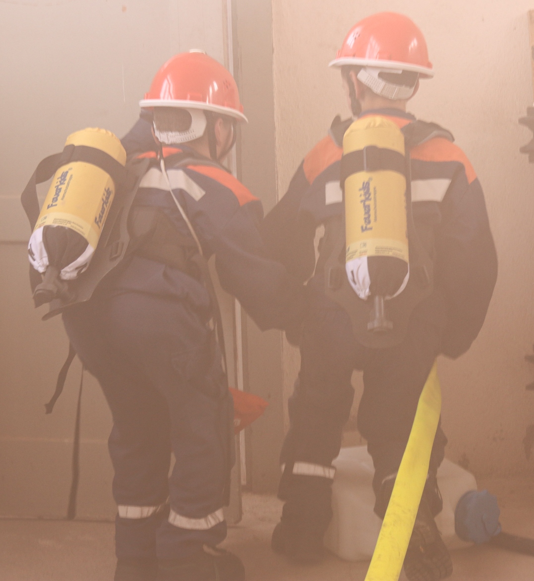 Zwei Mitglieder der Jugendfeuerwehr mit Atemschutzbehältergeräten Atrappen in einen vernebelten Raum